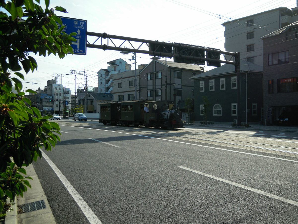 Small steam-style Botchan train running on a tram line along a wide street in Matsuyama