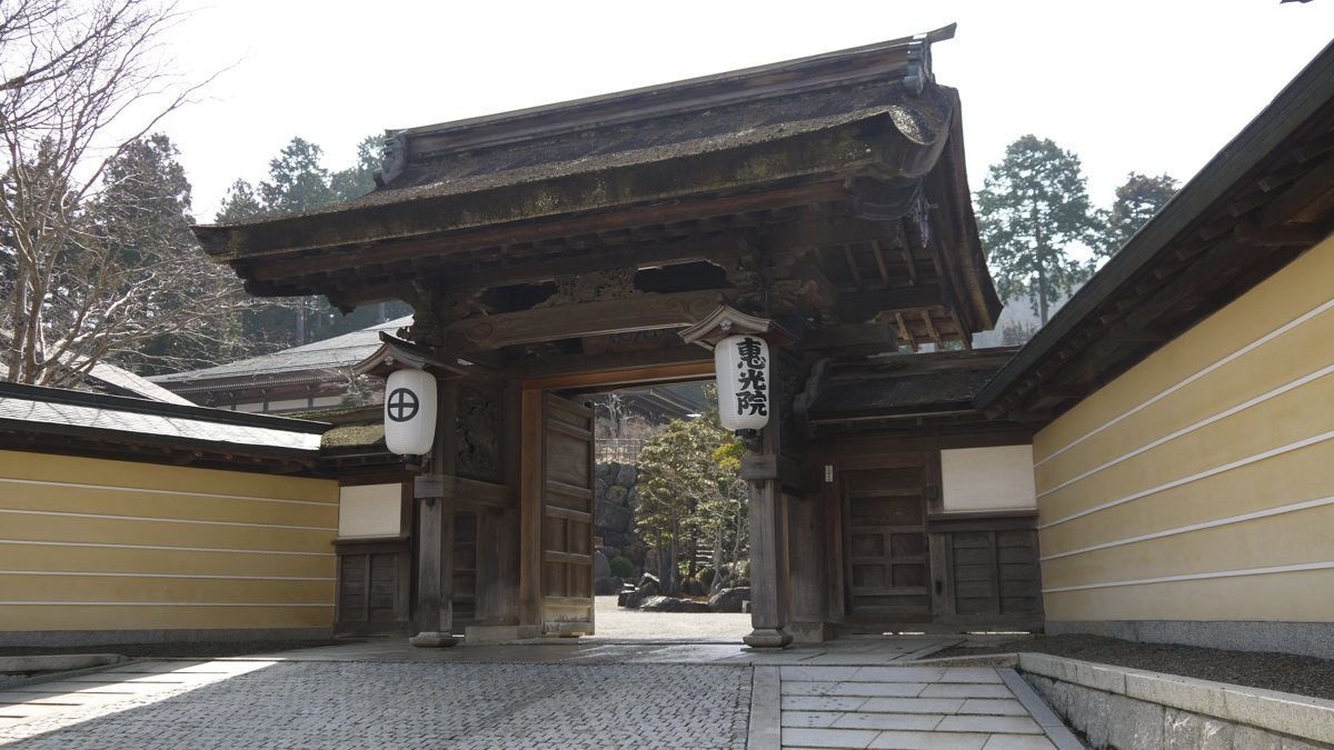 A wooden temple gate with white lanterns between plastered walls