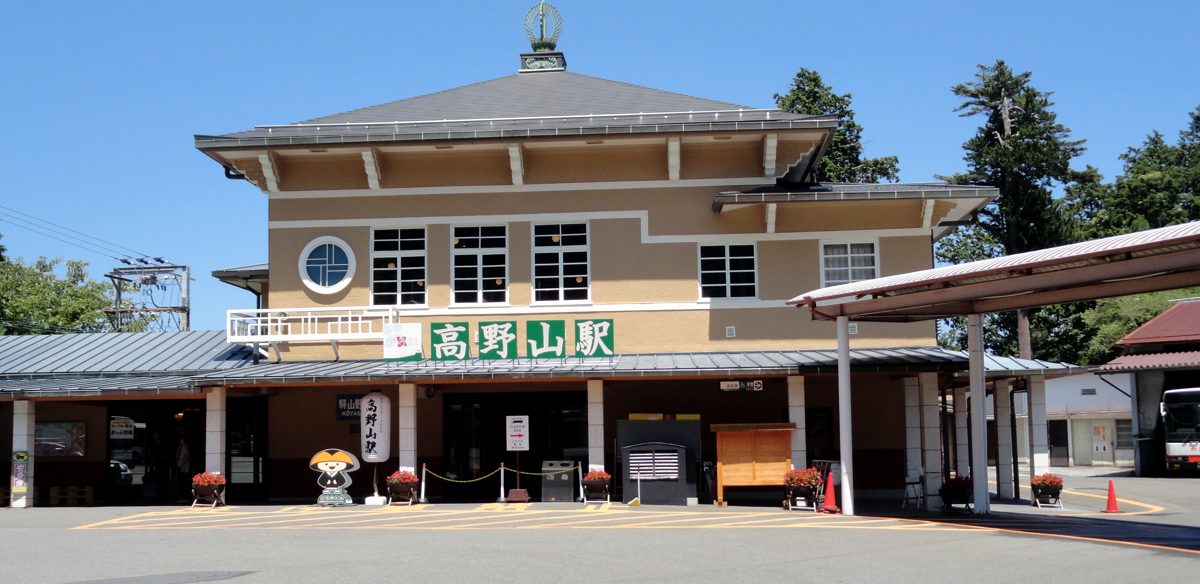 A two-story station building with a green sign on a sunny day