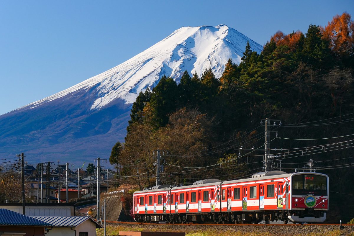 A red and white Fujikyu train running below a snow-capped Mount Fuji
