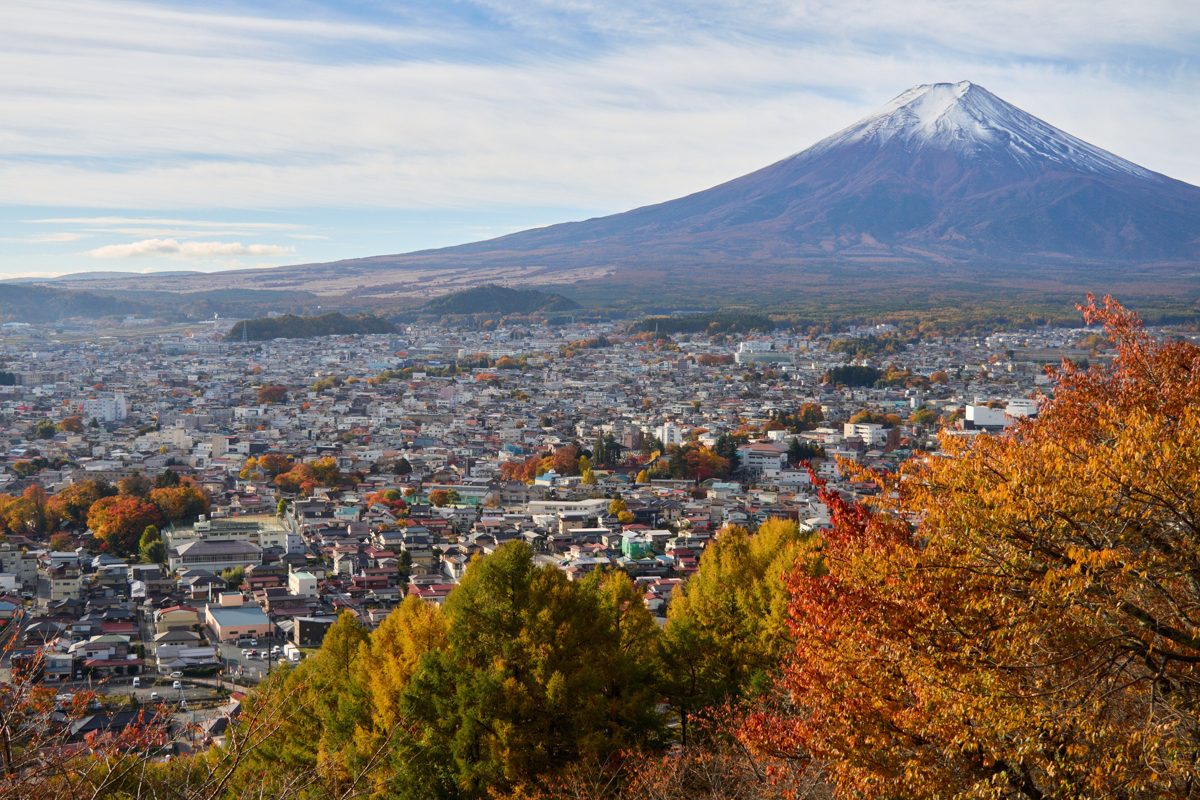 Mount Fuji rising behind the town of Fujiyoshida, with autumn trees in the foreground
