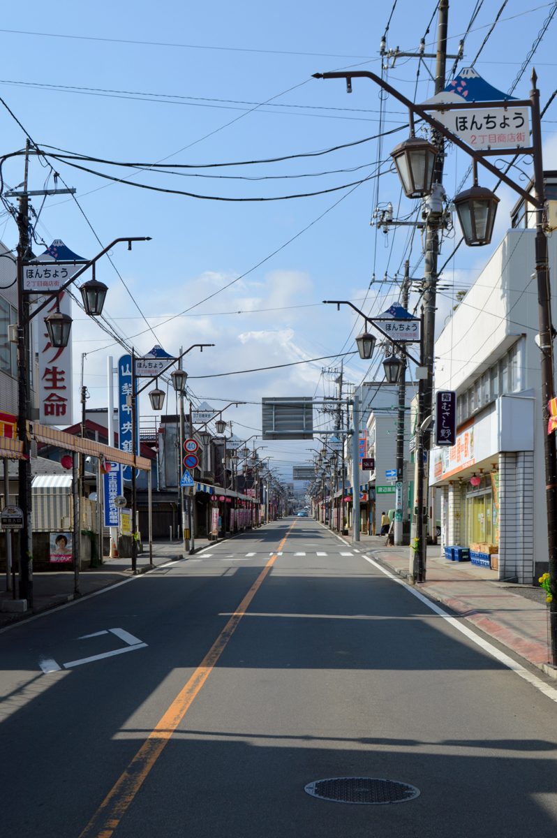 A quiet shopping street with streetlights and Japanese shop signs under a blue sky