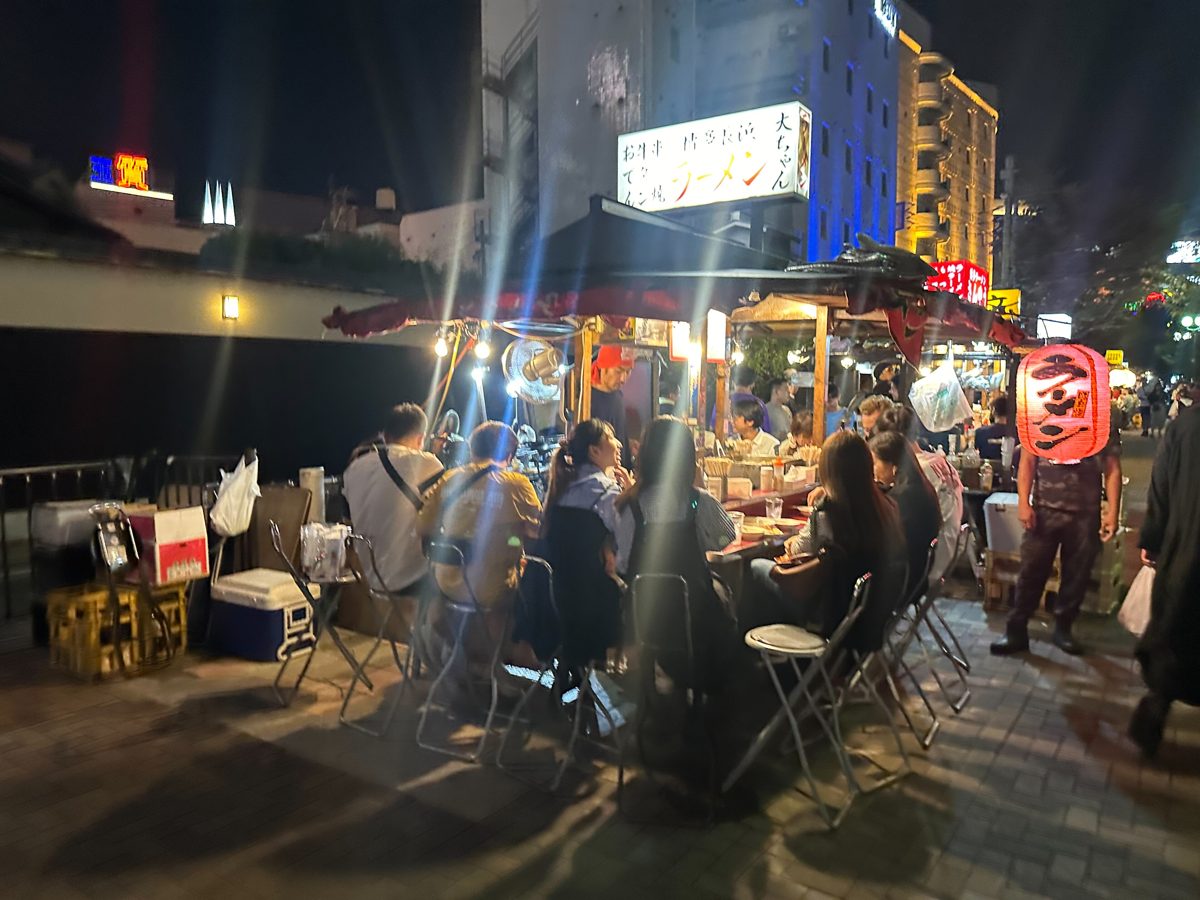 Street food stalls with lanterns and diners along a river at night