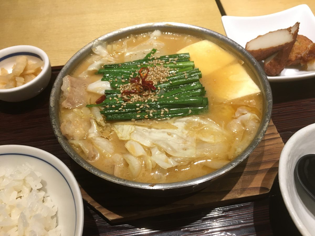 A shallow metal pot of offal hotpot topped with chives and sesame