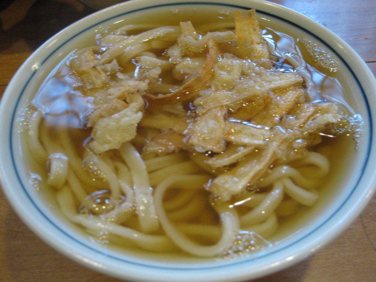 A bowl of udon topped with burdock tempura in a clear broth