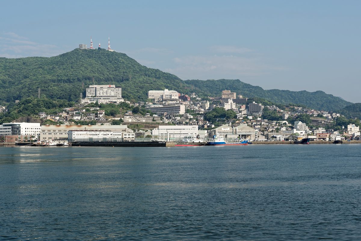 A green mountain with antennas on top rising behind a harbor