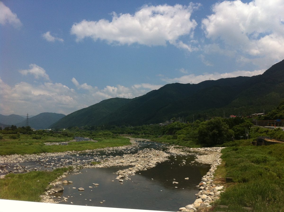 The Hida River flowing over stones between green mountains in Gero on a sunny day
