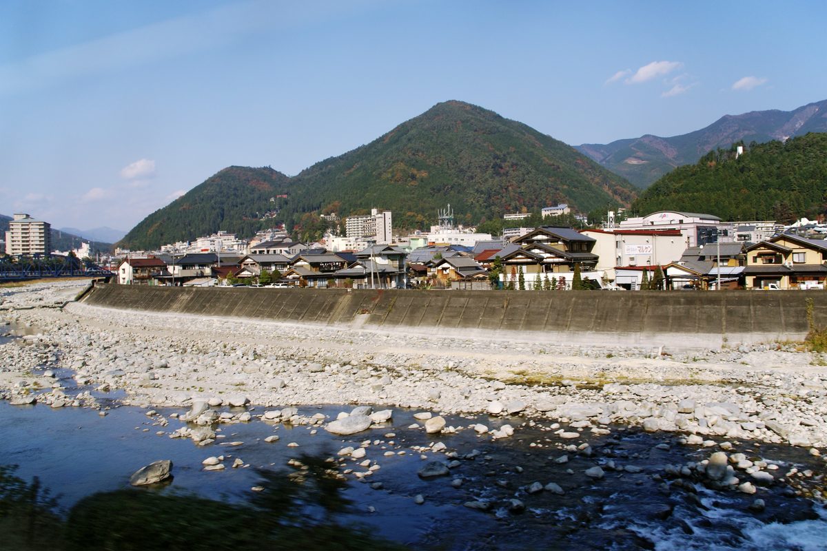 Gero Onsen town with mountains behind it and a wide stony riverbed in front, on a clear day