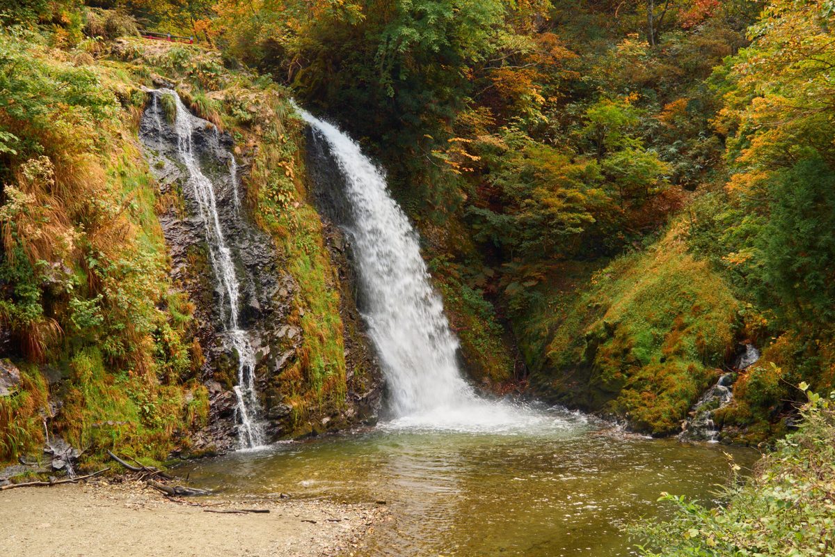 A waterfall falling into a shallow pool among green and orange autumn foliage
