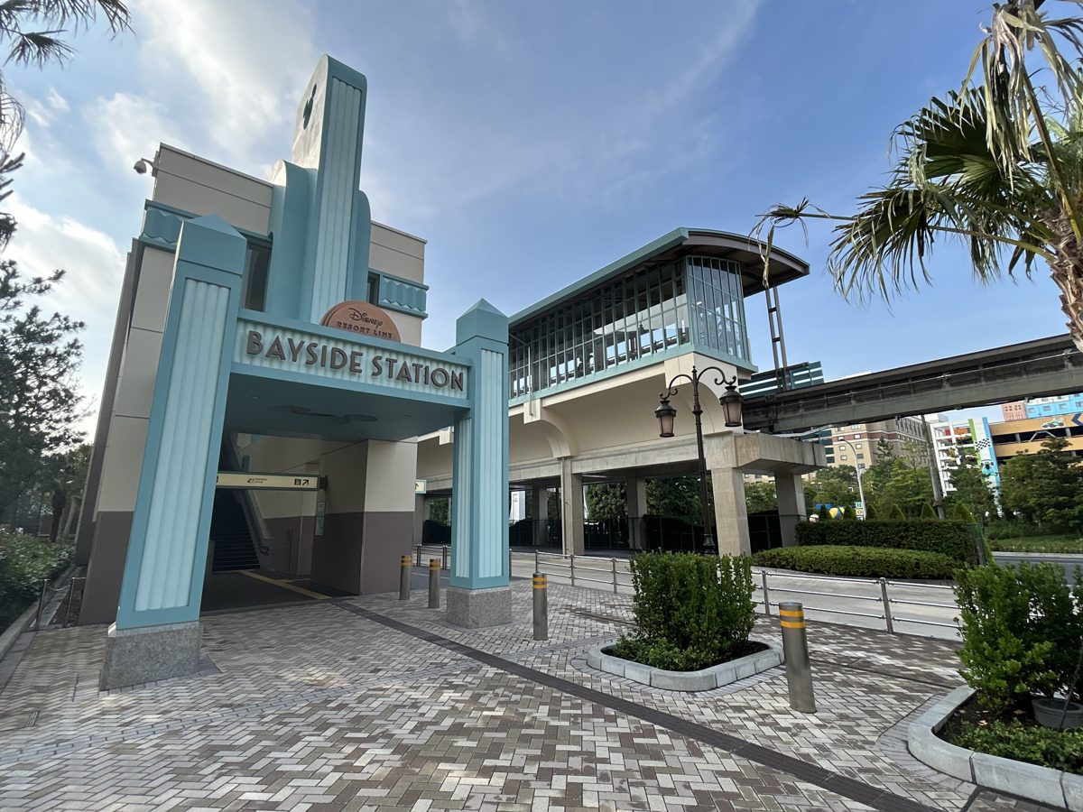 A station building with a tall rounded entrance and palm trees under a blue sky