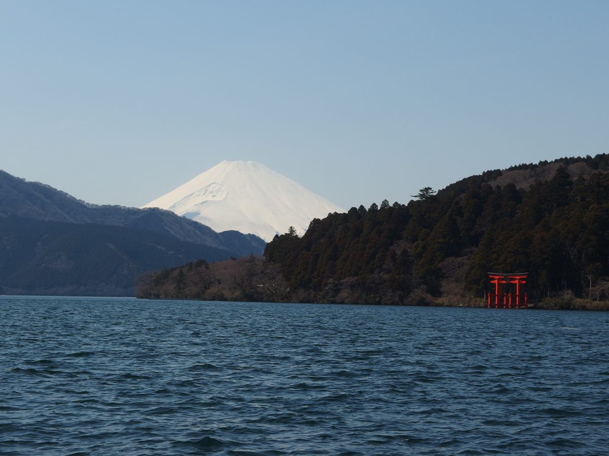 Lake Ashi with Mount Fuji behind it and a red torii gate on the shore, on a clear day