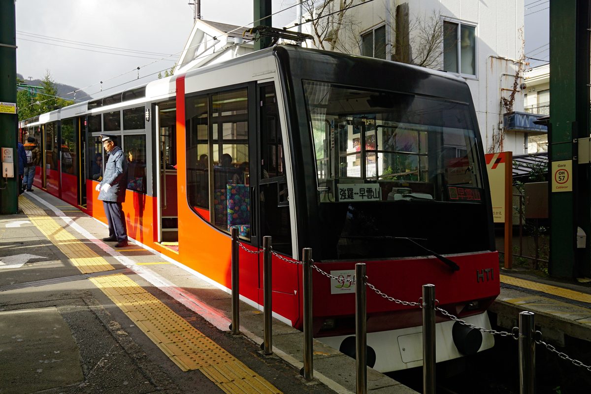 A red and orange cable car waiting at a station platform, with a destination sign for Gora and Sounzan