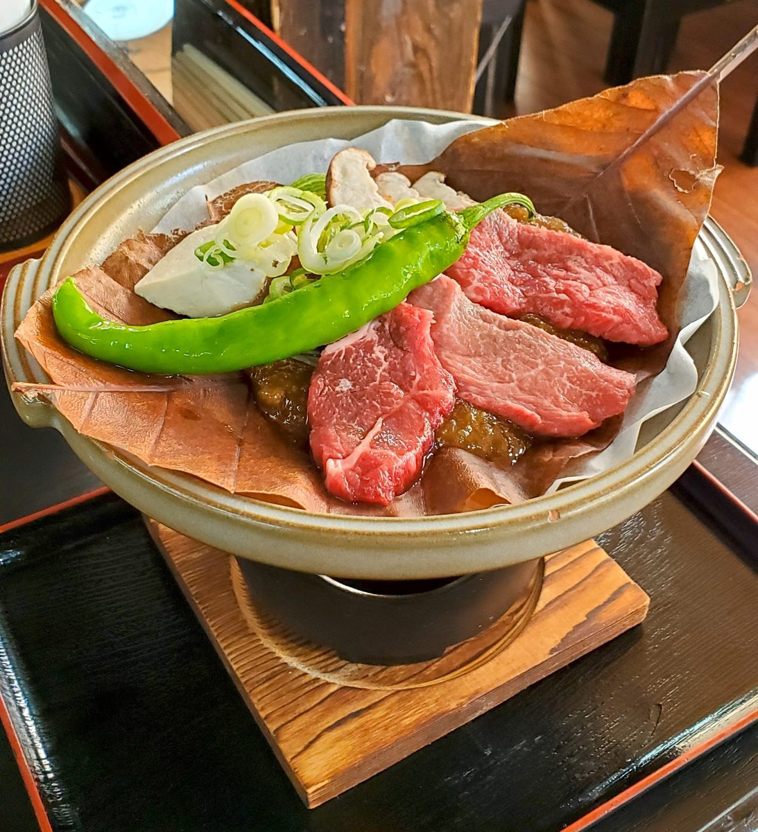 Slices of marbled Hida beef with leeks and a green pepper on hoba miso over a small burner
