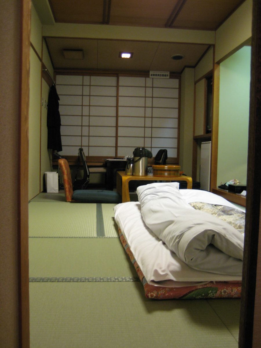 Tatami guest room with futon bedding laid out, a low table, and shoji screens