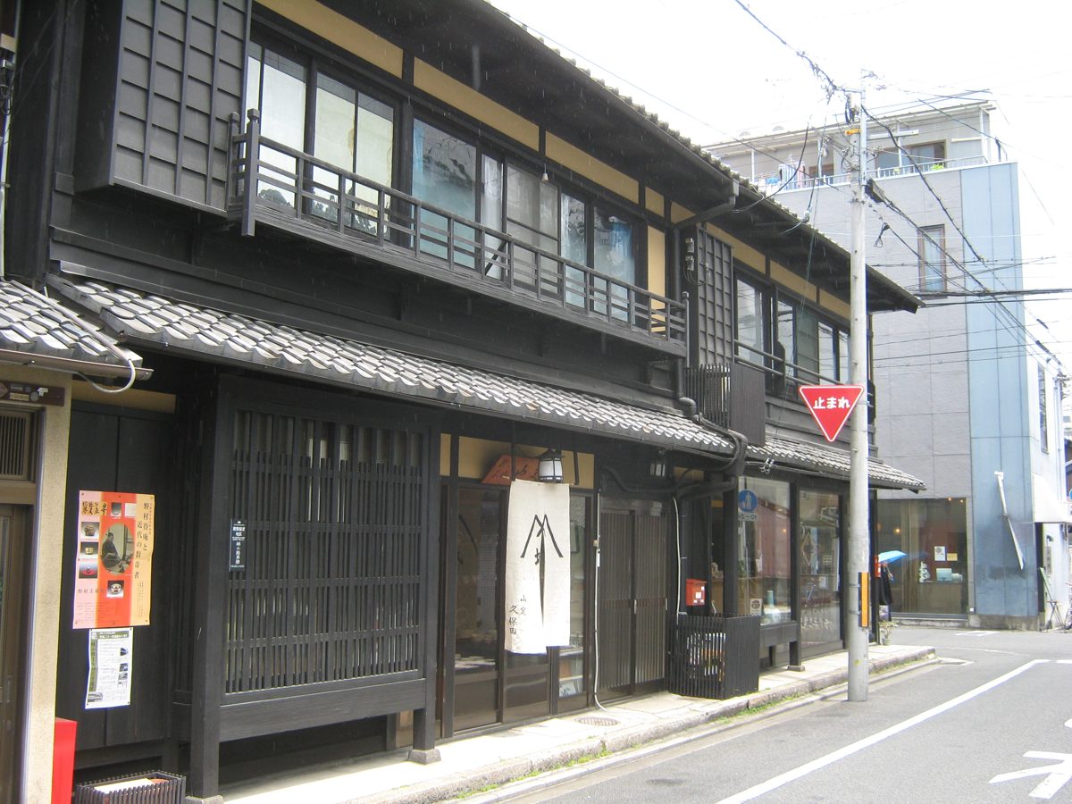 Two-story wooden machiya with lattice windows on a narrow Kyoto street