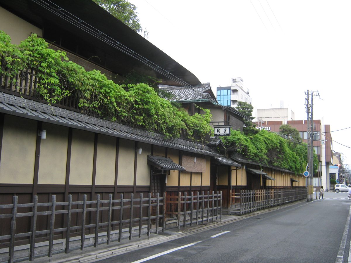 Long wooden facade of Hiiragiya ryokan with greenery along the roof, on a quiet street in Kyoto