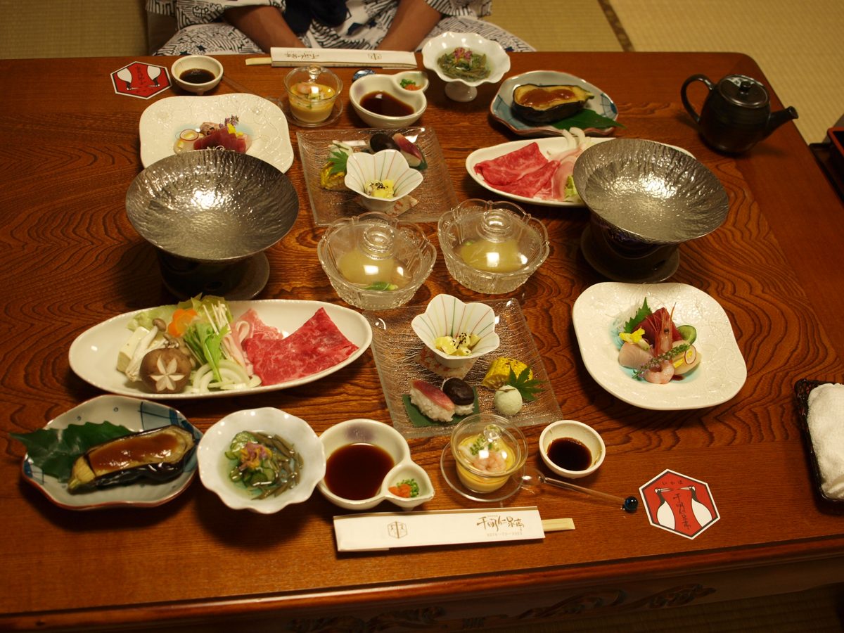 Many small dishes of a multi-course Japanese dinner arranged on a wooden table