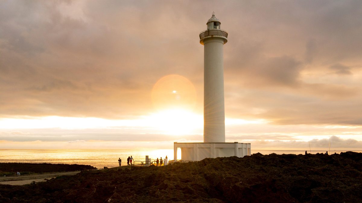 A white lighthouse on a rocky cape at sunset