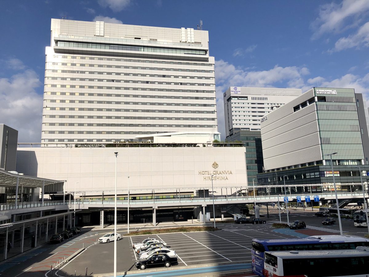 A tall white hotel block above a station plaza with a bus and taxi area