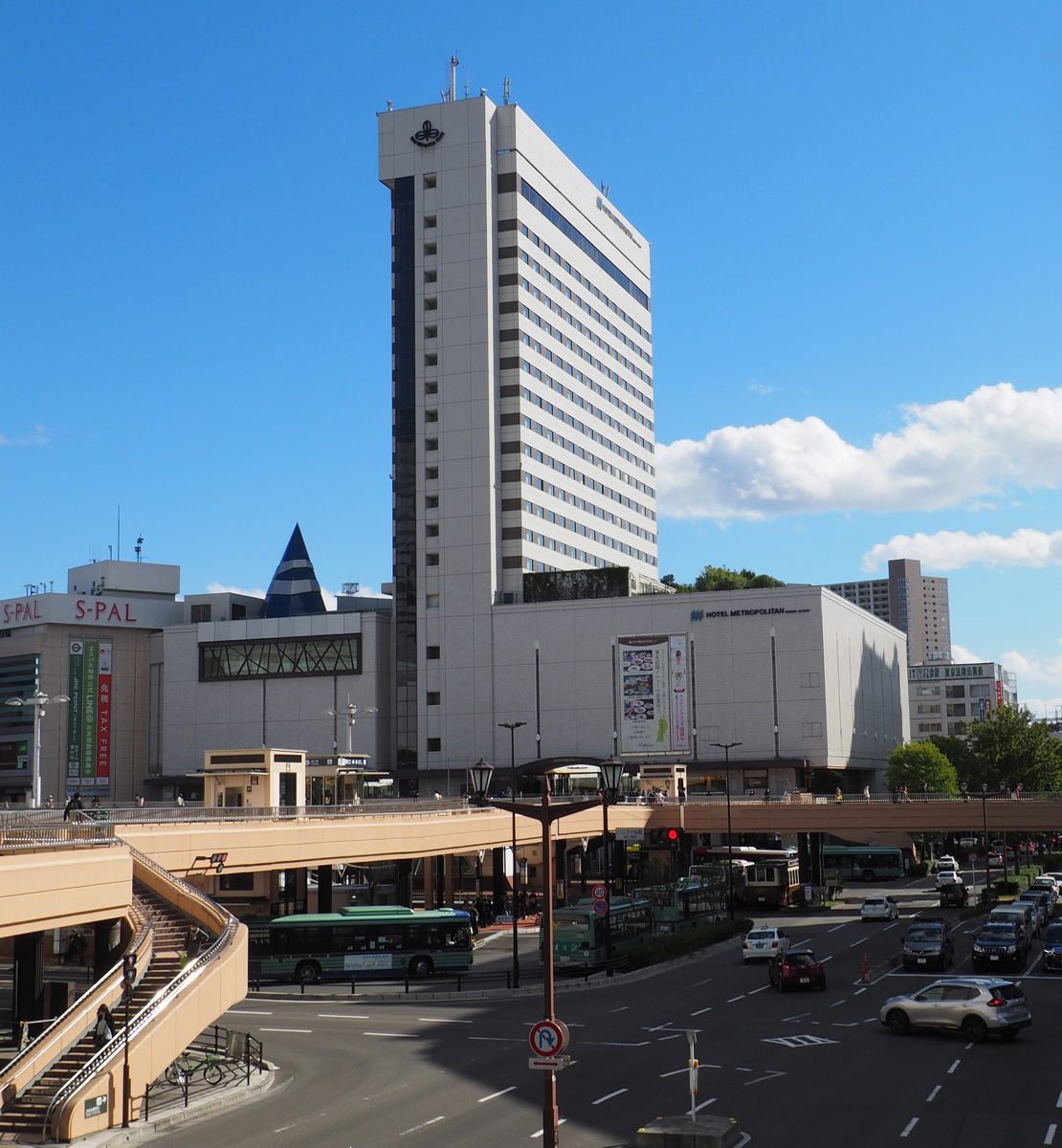 A white hotel tower beside a station building and a raised pedestrian deck