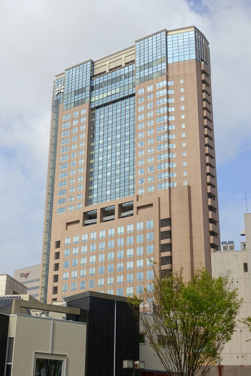 A tall brown and glass hotel tower under a partly cloudy sky