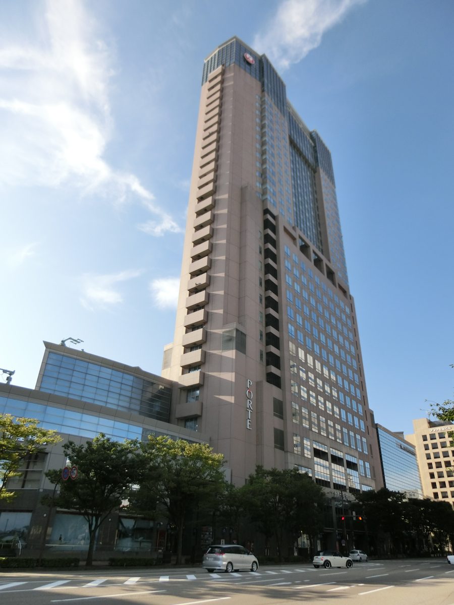 A slim high-rise tower with a glass-fronted low building at its base on a sunny day