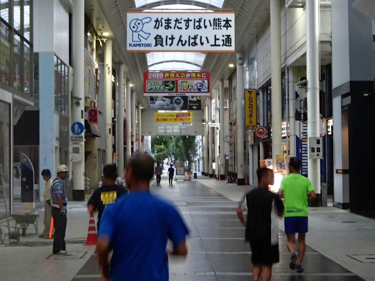 The covered Kamitori shopping arcade in Kumamoto with a large KAMITORI banner and people walking away from the camera