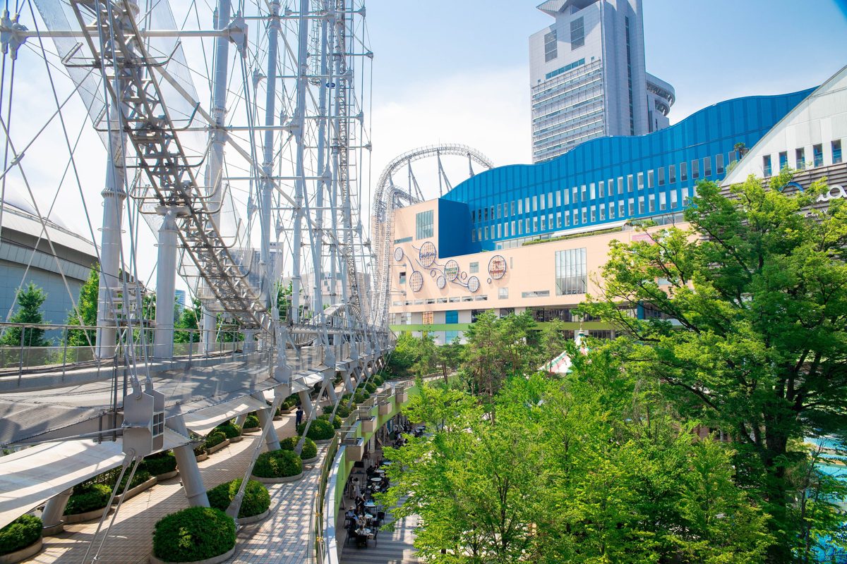 The Thunder Dolphin roller coaster track and leafy walkways at Tokyo Dome City on a sunny day