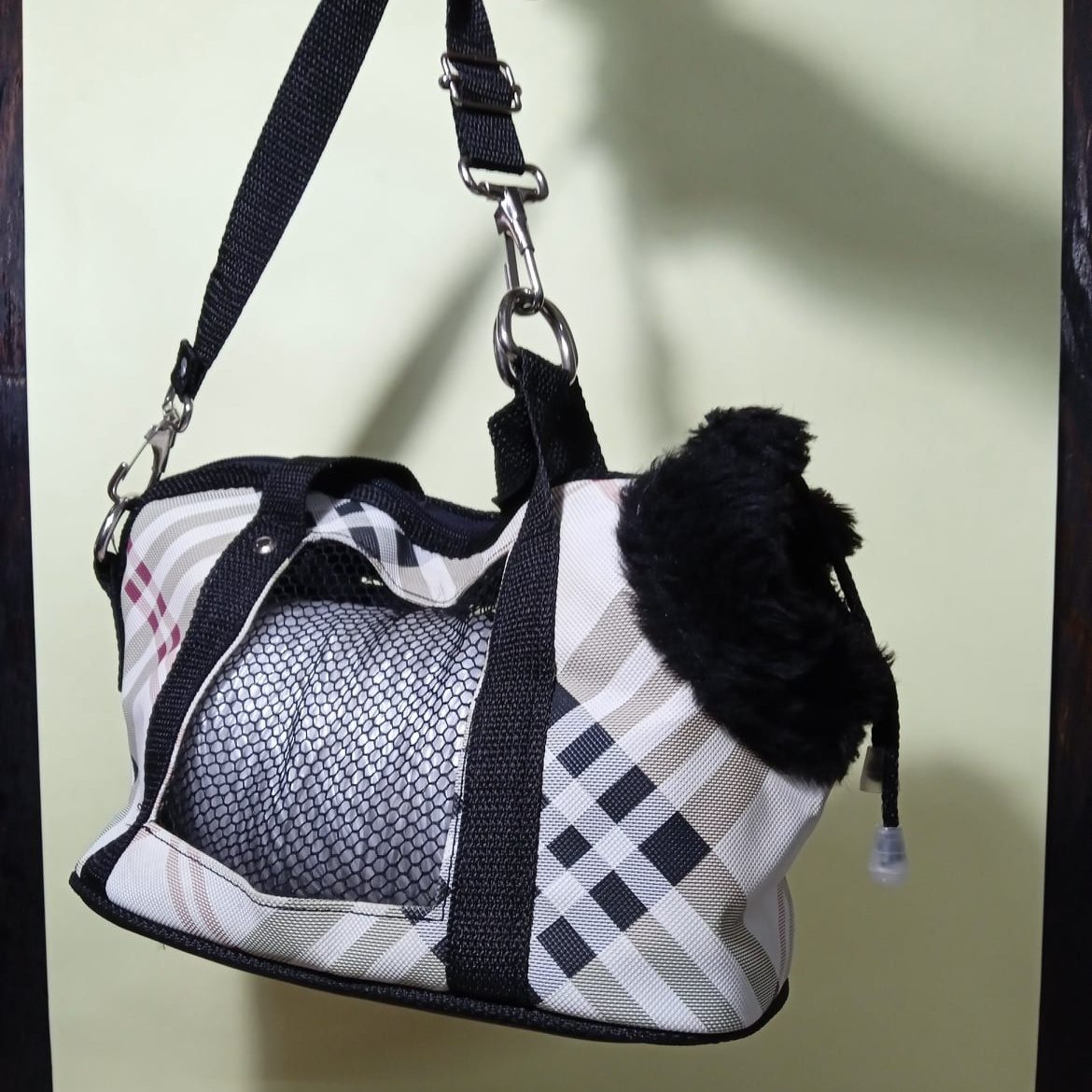 A plaid soft-sided carrier bag for a small dog hanging from its shoulder strap