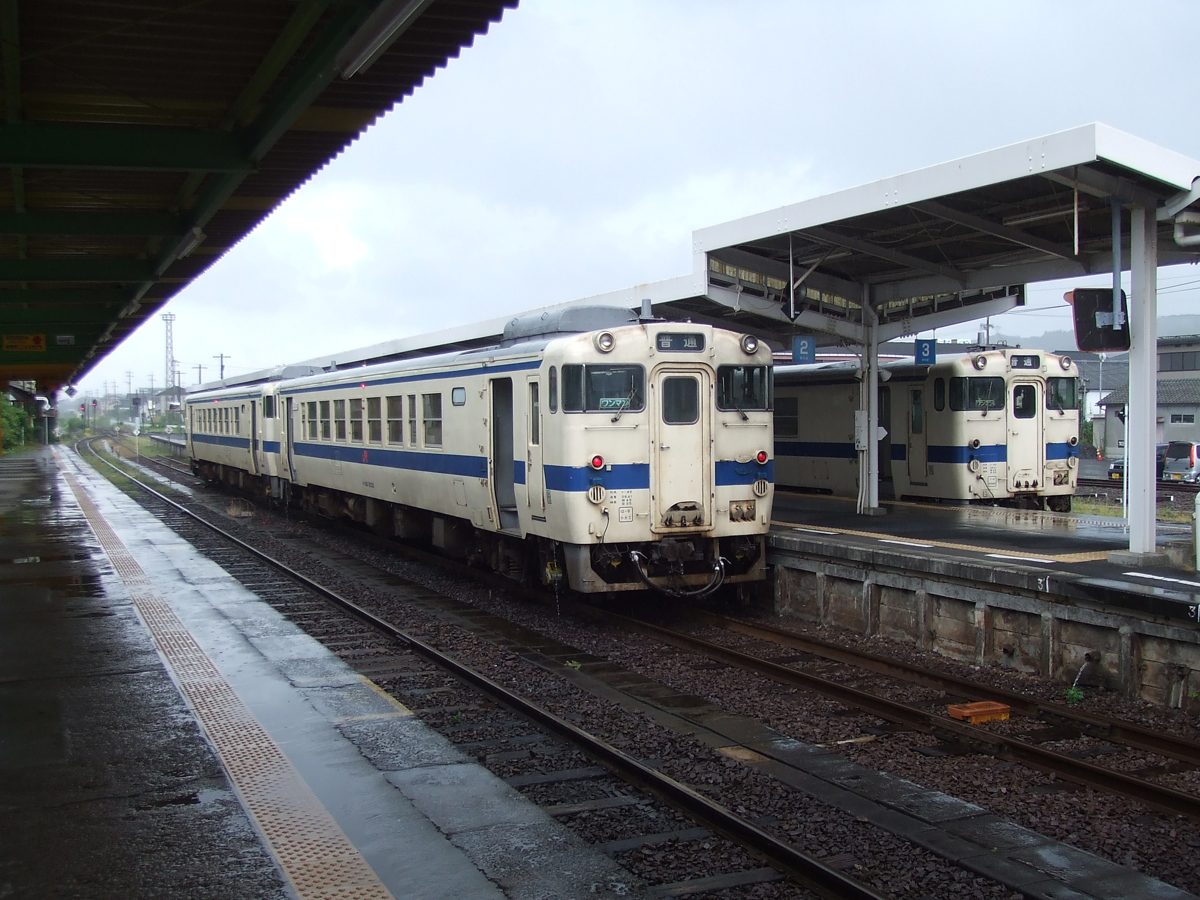 Two cream and blue local trains at a station platform on a rainy day