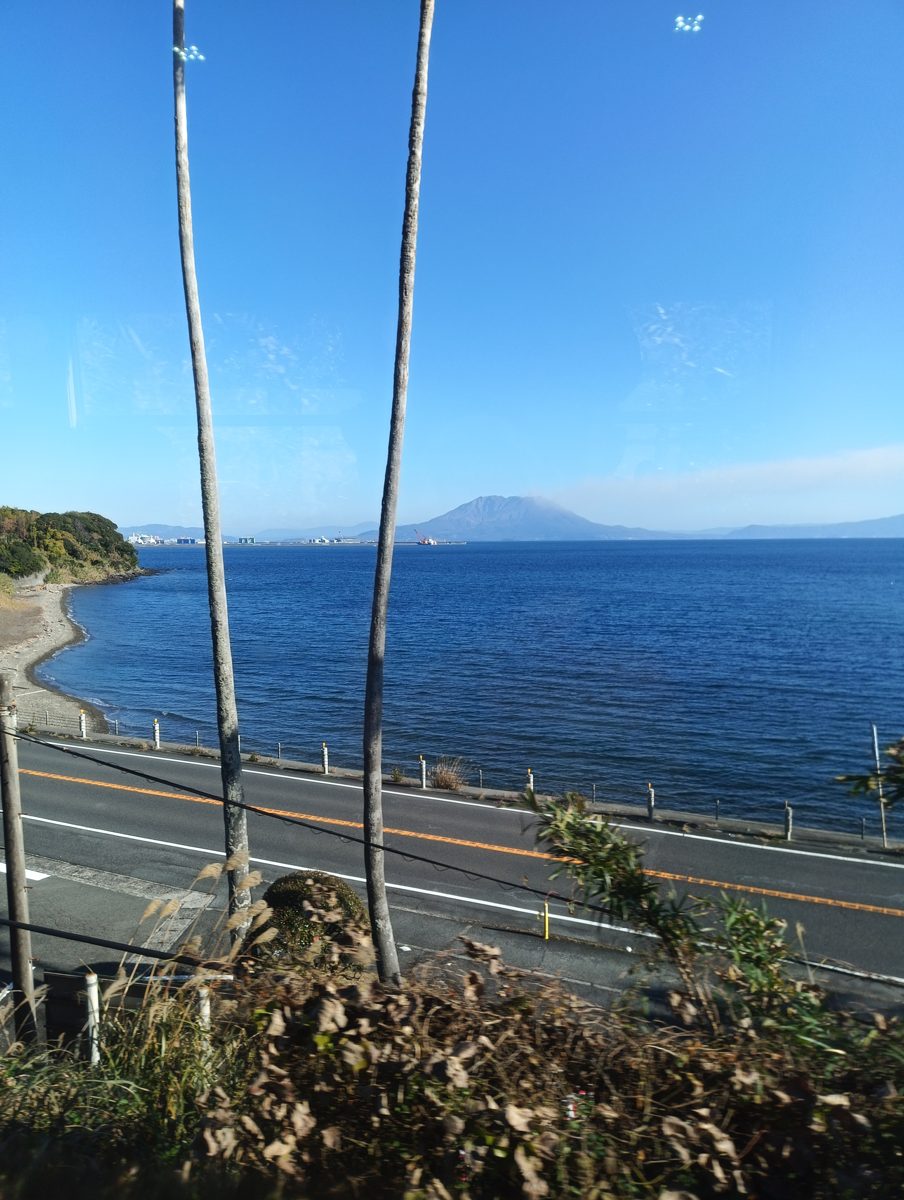 Blue sea and a coastal road seen through a window, with a mountain across the water