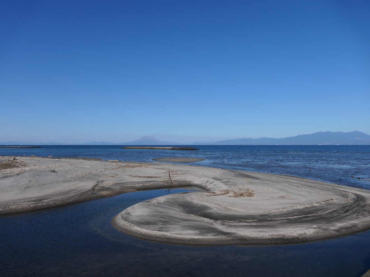A flat rock shelf curving into calm blue sea under a clear sky at Miyagahama beach
