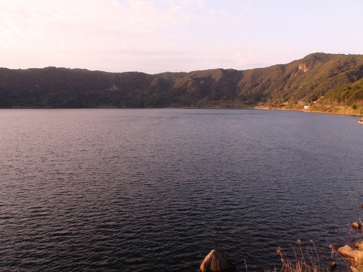 A calm lake surrounded by green forested hills in late afternoon light