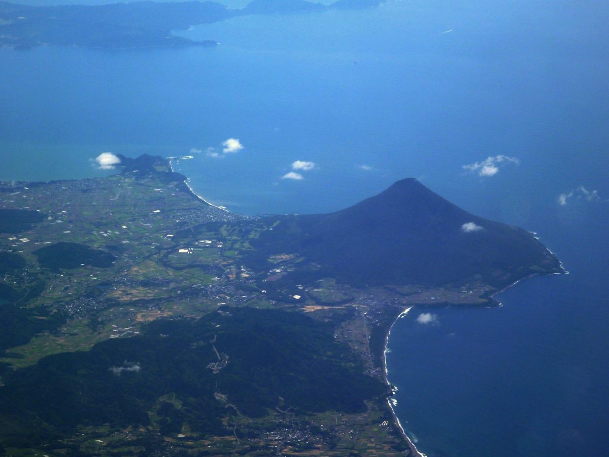 Aerial view of Mount Kaimon, a cone-shaped volcano on the coast, with blue sea and clouds