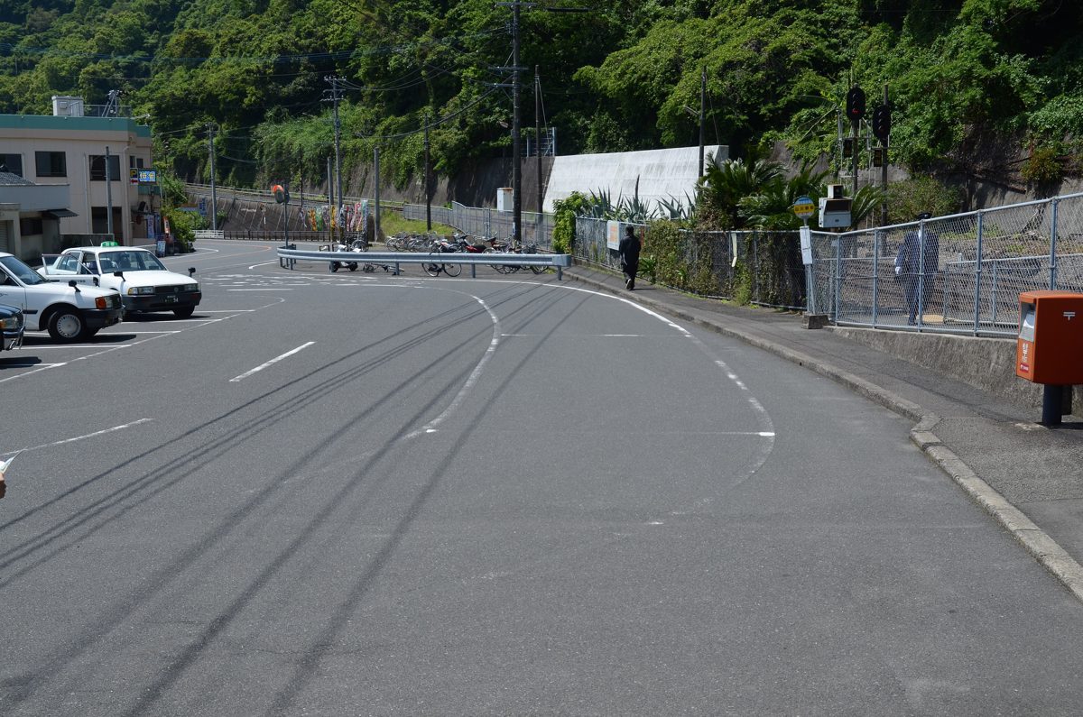 A road and parking area in front of a station, with trees on a hillside behind