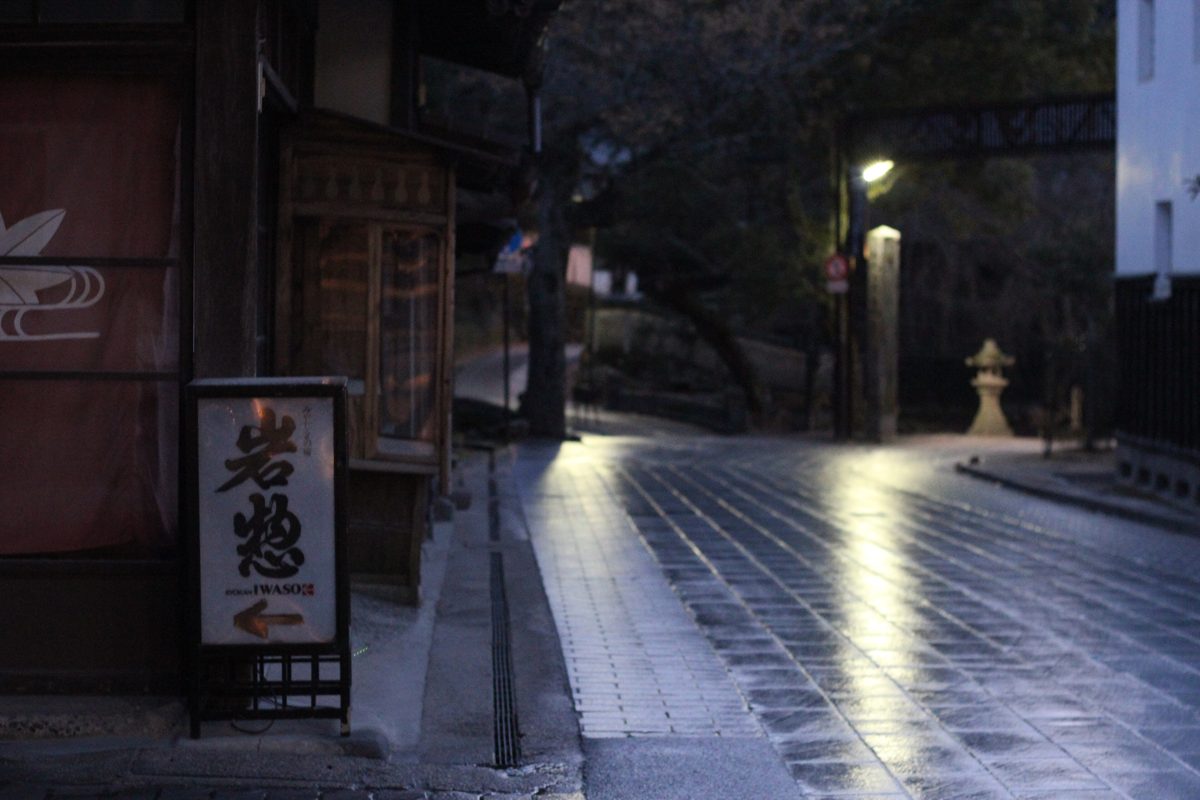 A sign reading Iwaso beside a wet stone-paved lane at night