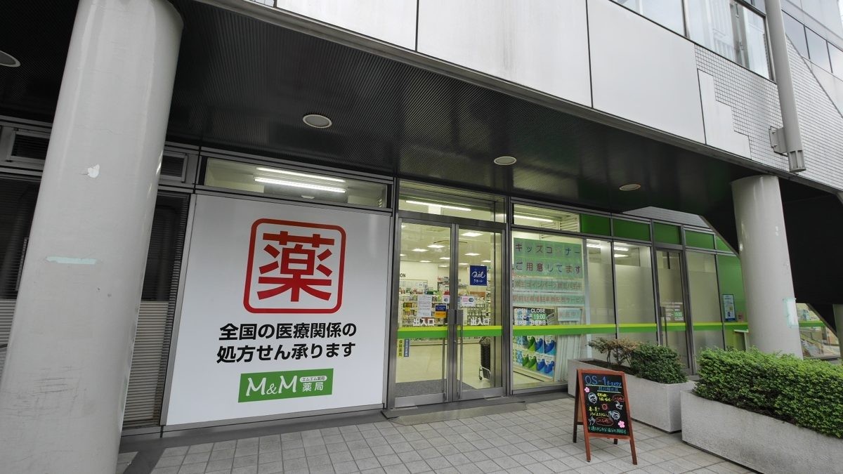 Entrance of an M&M pharmacy with a large red 薬 sign and a notice that it fills prescriptions