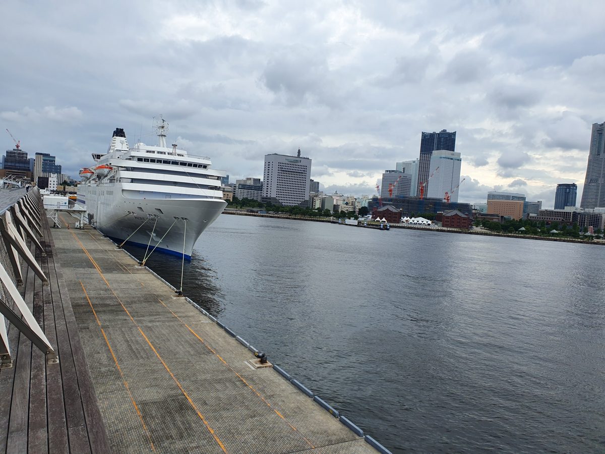A white cruise ship moored at the wooden pier of Osanbashi with the Yokohama skyline behind