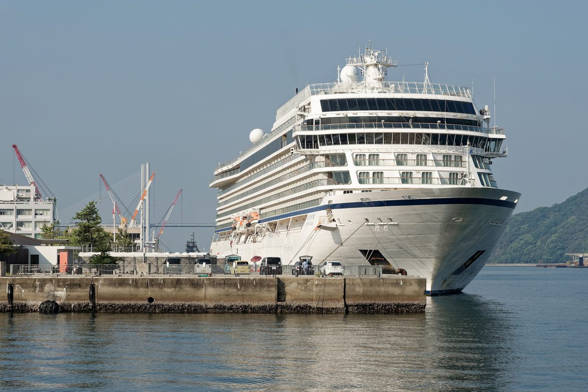 A large white cruise ship moored at a quay in the Port of Nagasaki on a clear morning