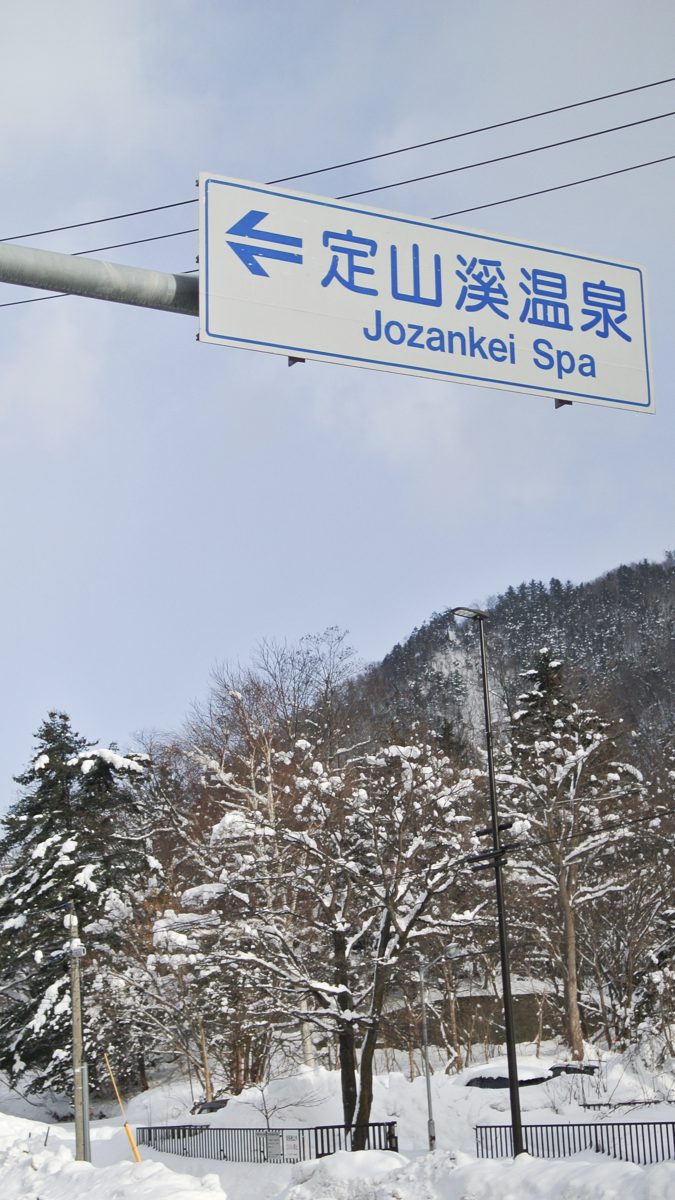 A blue road sign reading Jozankei Spa beside snowy trees