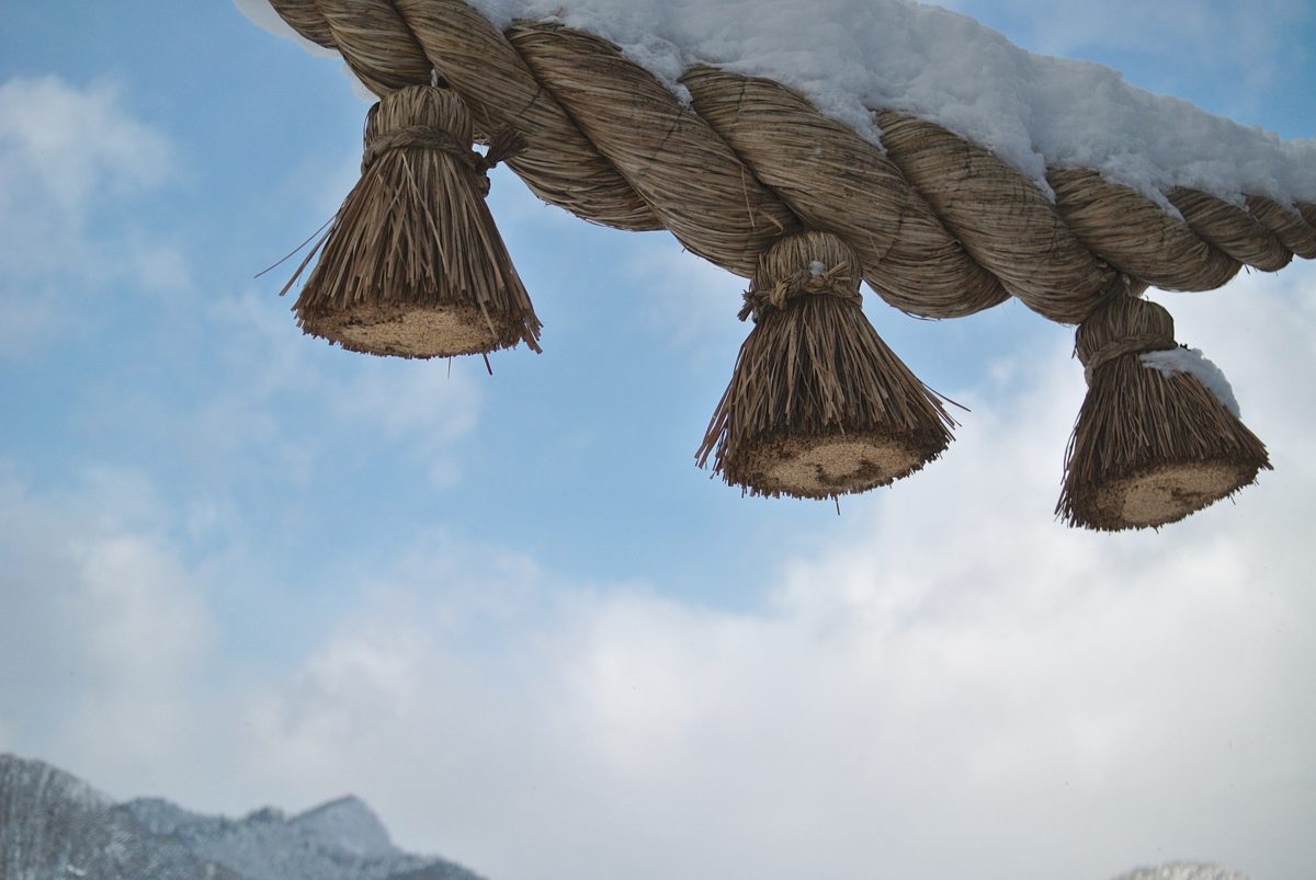 A thick straw rope with tassels, topped with snow, against a blue sky