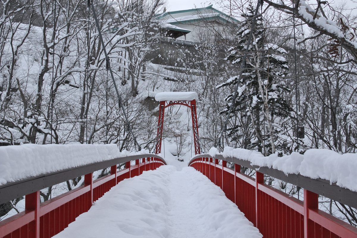 A red footbridge covered in snow among snowy trees at Jozankei Onsen