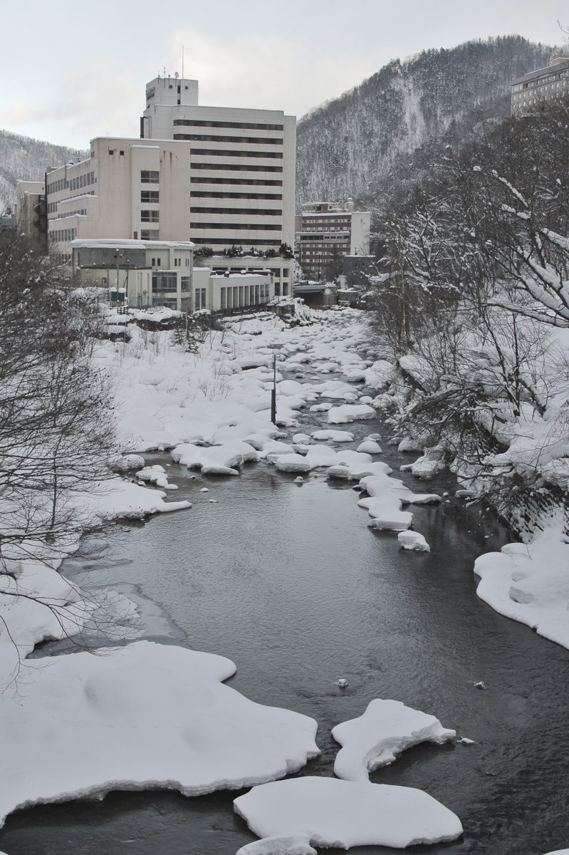 A snowy river valley with hotel buildings in the distance at Jozankei Onsen