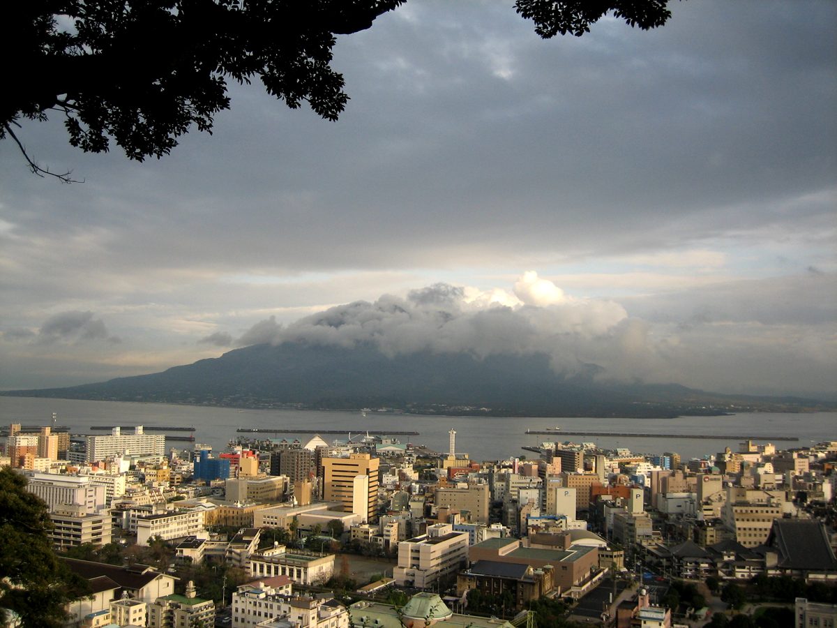 Sakurajima volcano under cloud across the bay, with the buildings of Kagoshima city in the foreground