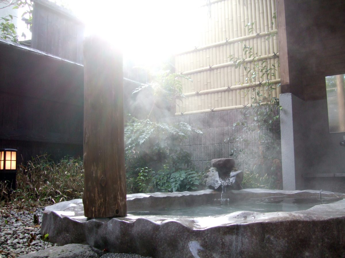 A steaming open-air stone bath with a wooden pillar and bamboo fence