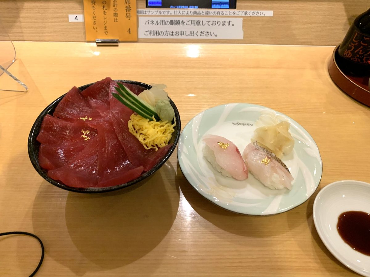 Tuna rice bowl and two pieces of sushi topped with gold leaf on a restaurant counter