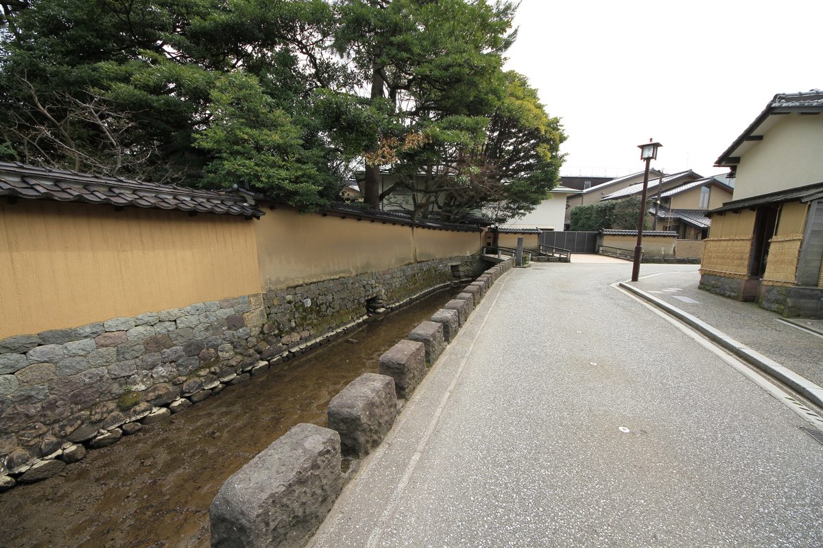 A quiet lane beside long earthen walls with a tiled top and a narrow stone canal