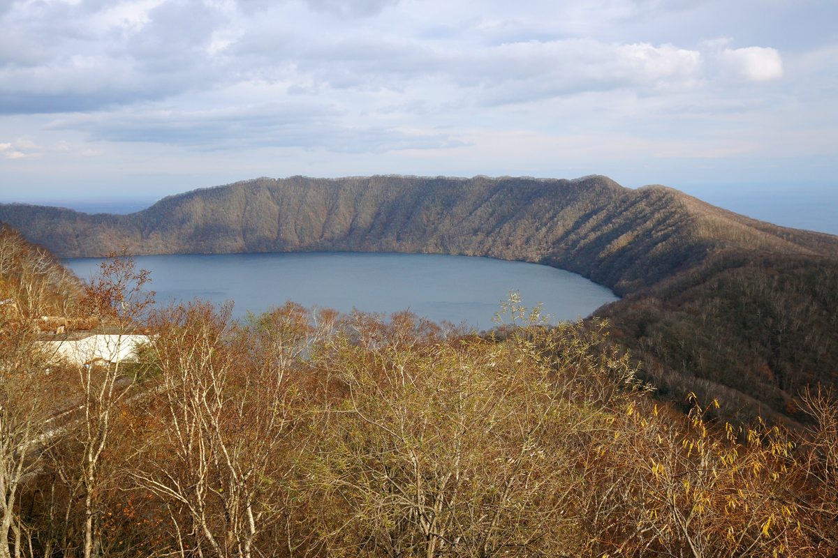 Lake Kuttara, a round crater lake, seen from a hillside with autumn trees