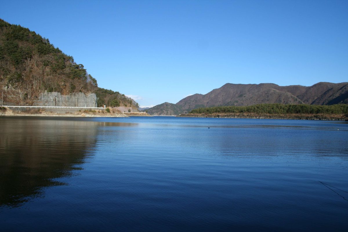 Calm blue lake water with wooded hills and a clear sky