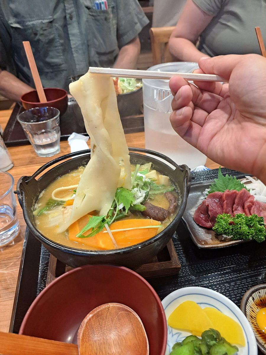 A bowl of thick hoto noodles in miso soup lifted with chopsticks